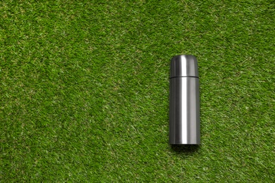 Modern silver thermos on green grass, top view. Space for text