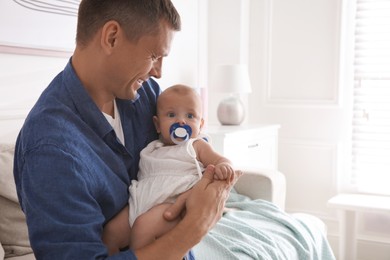 Photo of Happy father holding his cute little baby with pacifier at home, space for text
