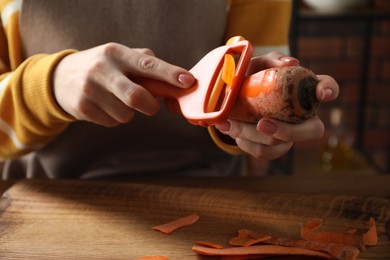 Photo of Woman peeling fresh carrot at wooden table indoors, closeup