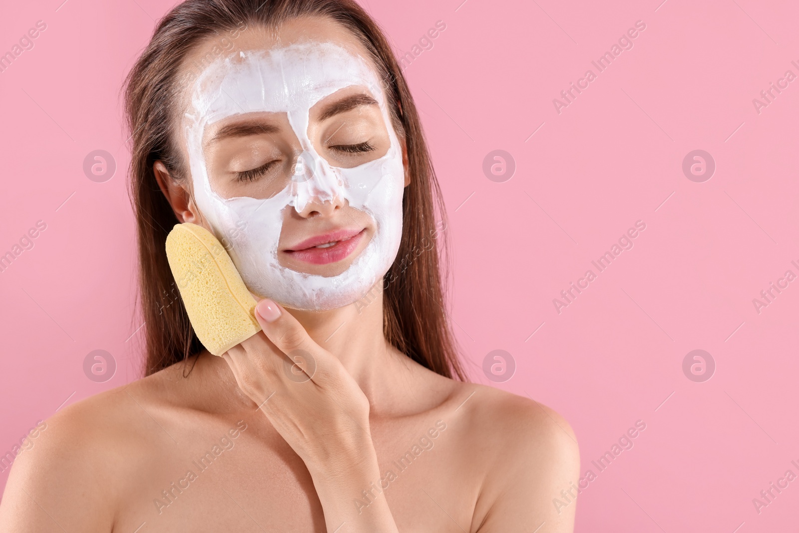 Photo of Happy young woman with face mask and sponge on pink background. Space for text