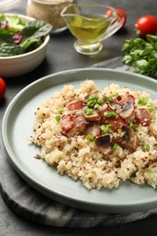 Photo of Plate of tasty quinoa porridge with fried bacon, mushrooms and green onion on table, closeup