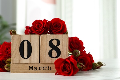 Photo of Wooden block calendar with date 8th of March and roses on table indoors, space for text. International Women's Day