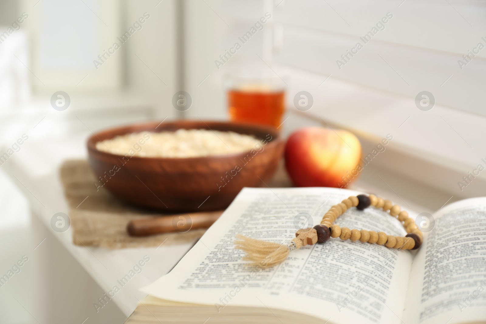 Photo of Holy Bible with prayer beads on window sill indoors, closeup. Great Lent season