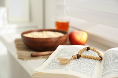 Photo of Holy Bible with prayer beads on window sill indoors, closeup. Great Lent season