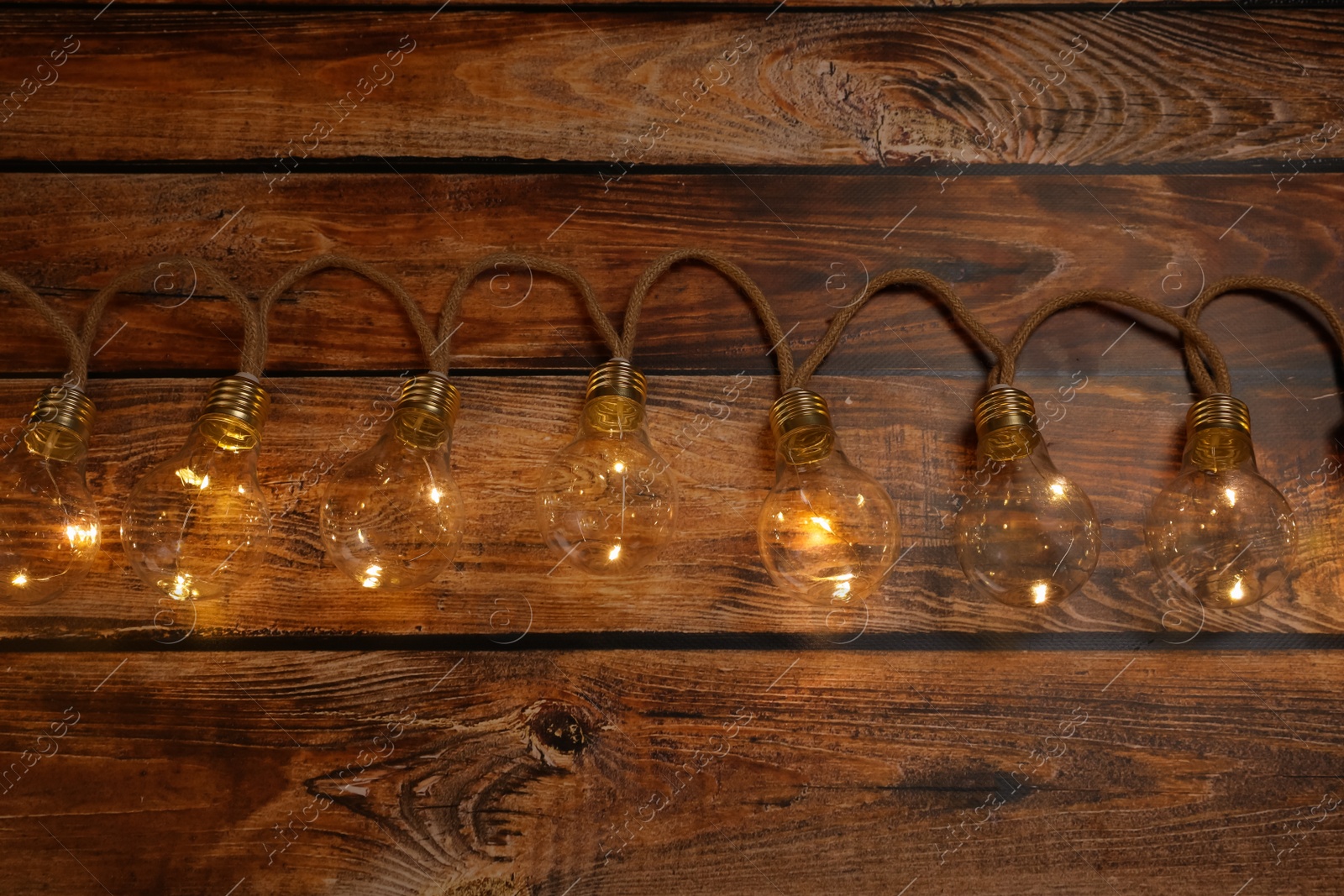 Photo of String lights with lamp bulbs on wooden table, top view