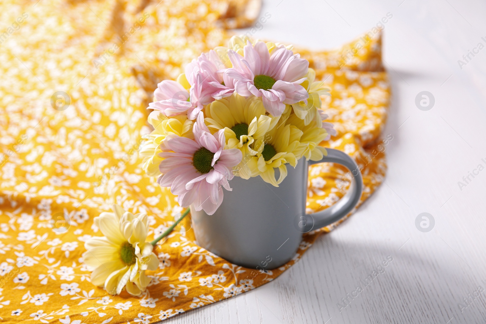 Photo of Bouquet of beautiful flowers in cup on orange printed cloth