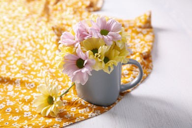 Photo of Bouquet of beautiful flowers in cup on orange printed cloth