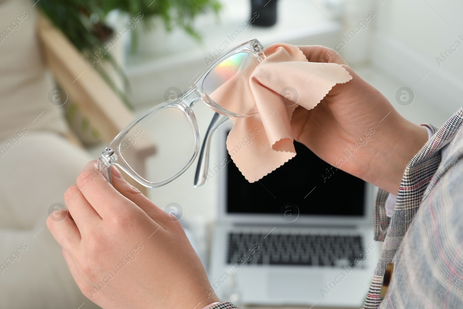 Photo of Woman cleaning glasses with microfiber cloth at home, closeup