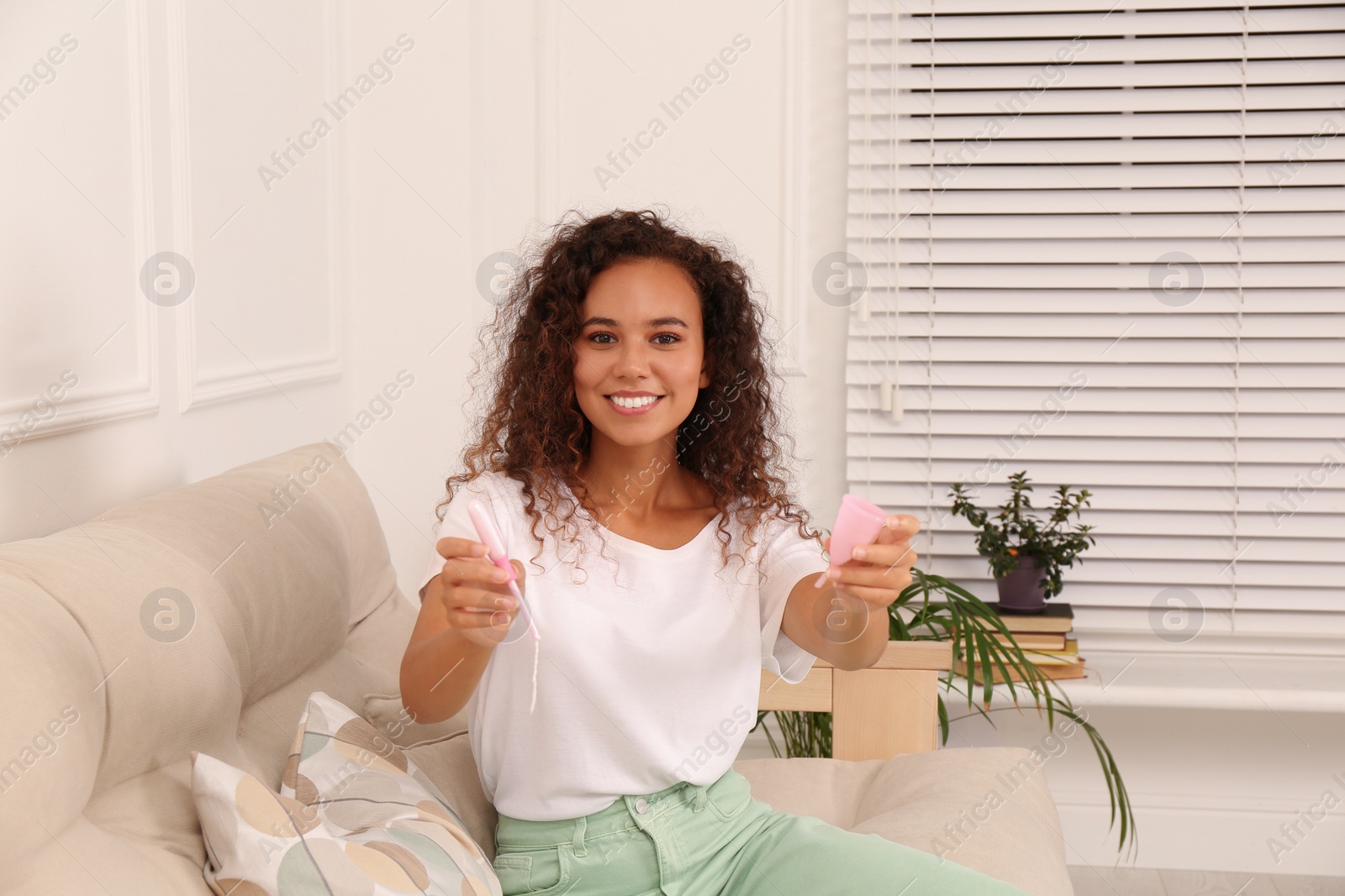 Photo of Young African American woman with menstrual cup and tampon at home