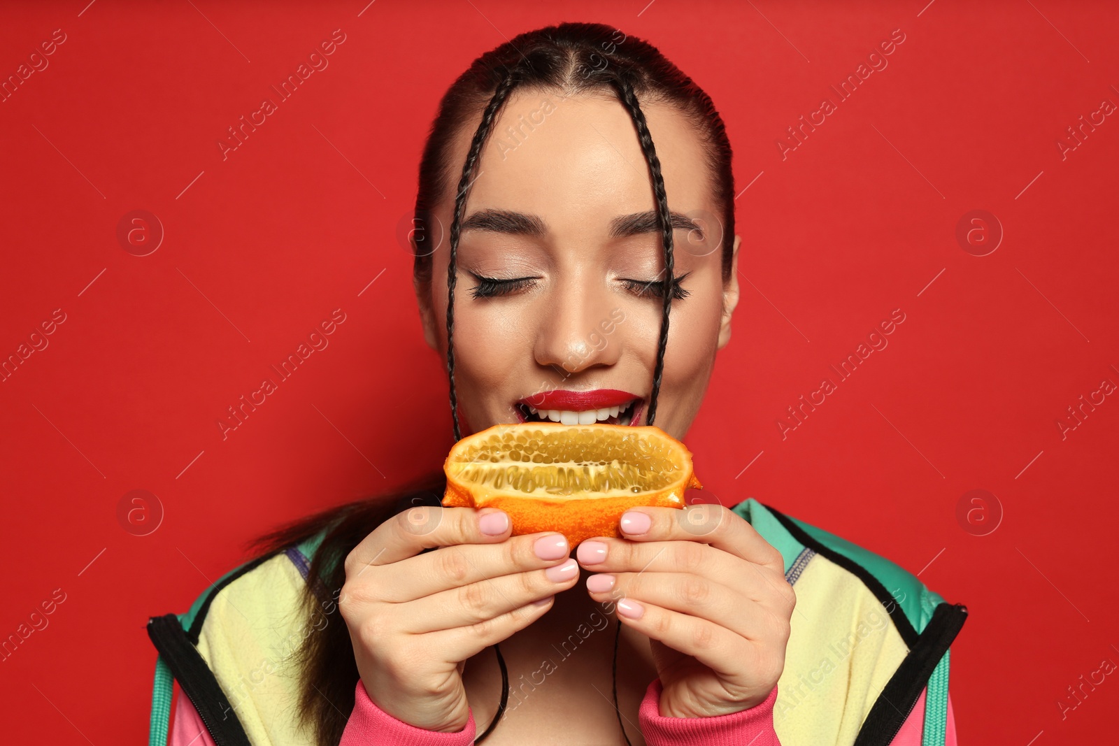 Photo of Young woman with fresh kiwano on red background. Exotic fruit