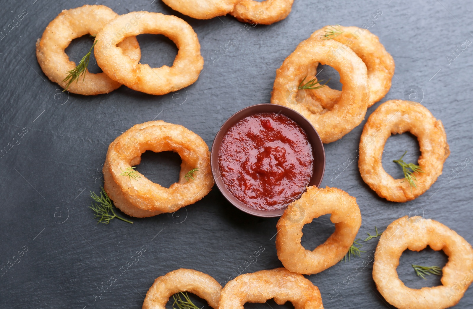 Photo of Slate plate with fried onion rings and bowl of sauce, top view