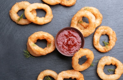 Photo of Slate plate with fried onion rings and bowl of sauce, top view