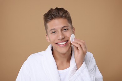 Handsome man cleaning face with cotton pad on beige background