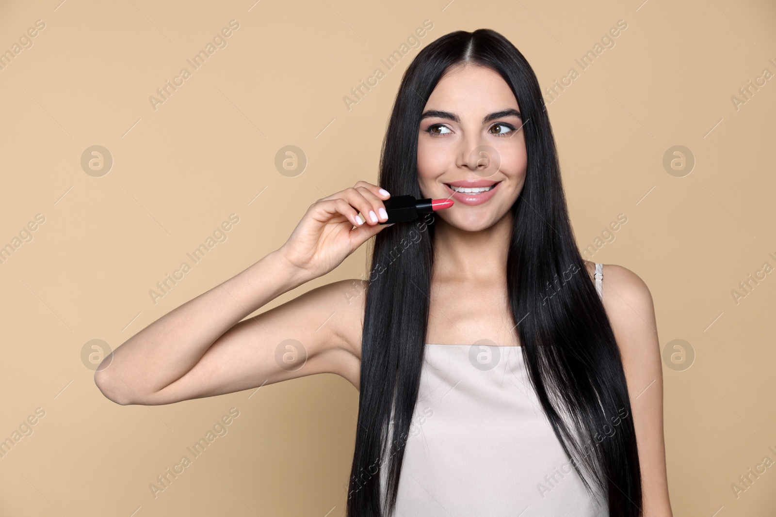 Photo of Young woman with beautiful makeup holding nude lipstick on beige background