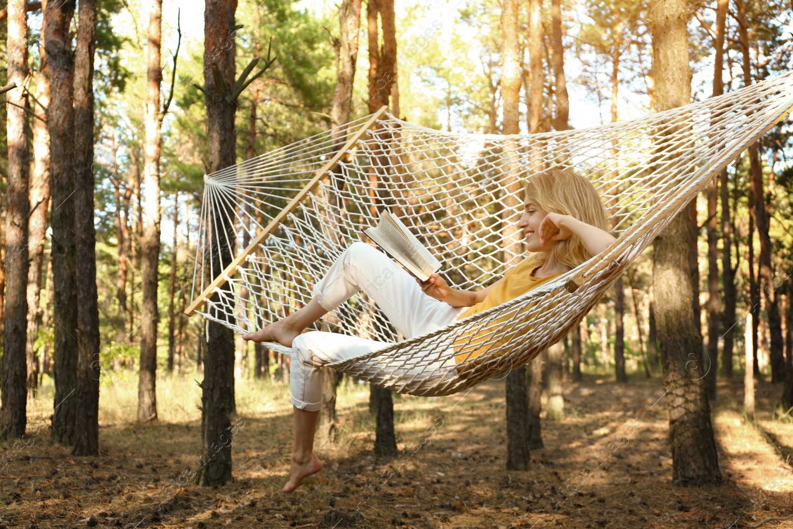 Photo of Happy young woman with book relaxing in hammock outdoors on summer day