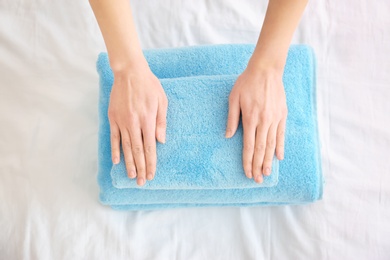 Photo of Woman folding clean towels on bed, closeup