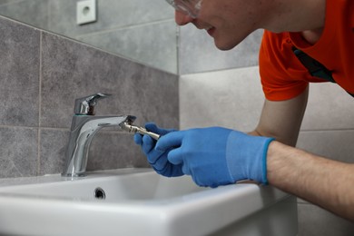 Plumber repairing faucet with spanner in bathroom, closeup