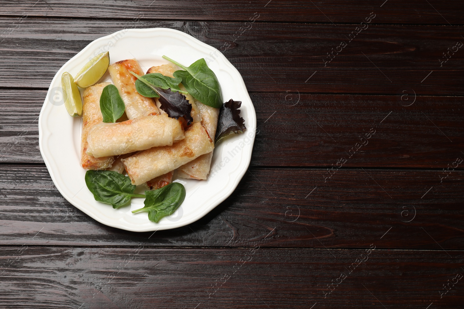 Photo of Plate with tasty fried spring rolls, spinach and lime on wooden table, top view. Space for text