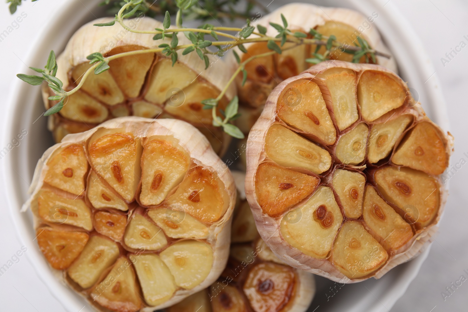 Photo of Heads of fried garlic and thyme in bowl on table, top view