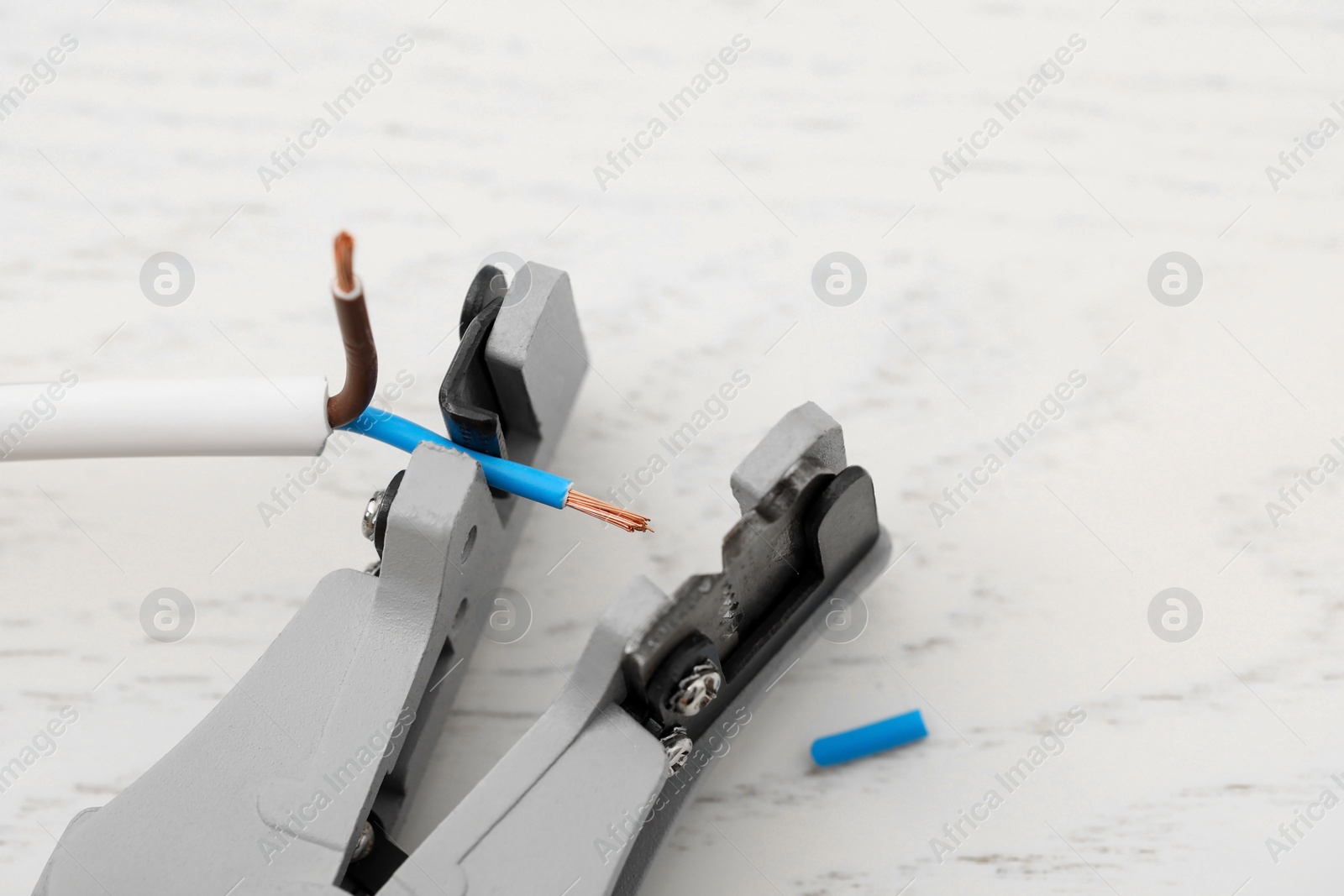 Photo of Cutters and stripped wire on white wooden table, closeup. Space for text