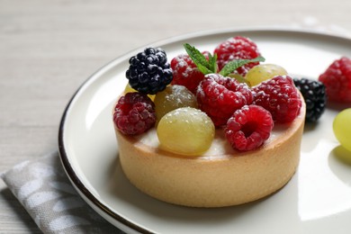 Delicious tartlet with berries on light wooden table, closeup