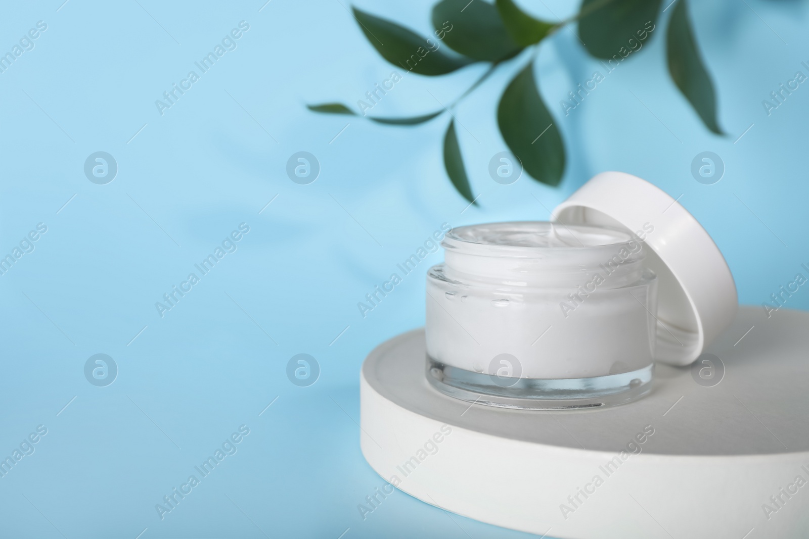 Photo of Jar of body cream with white stand on turquoise background. Space for text