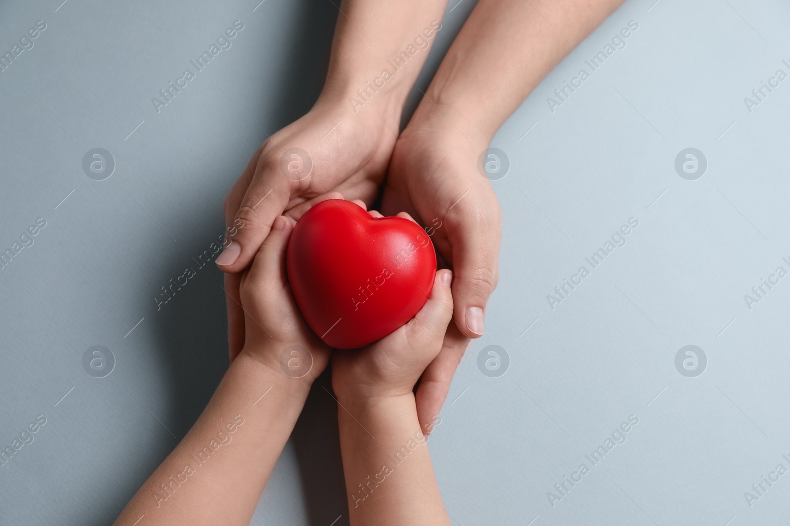 Photo of Mother and her child holding red decorative heart on gray background, top view