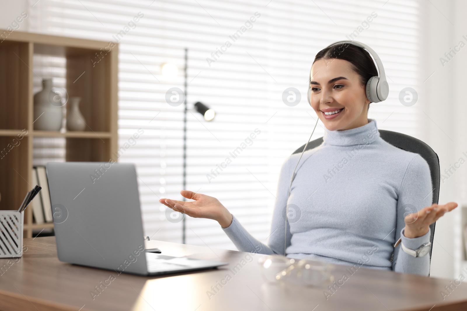 Photo of Young woman in headphones using video chat during webinar at table in office