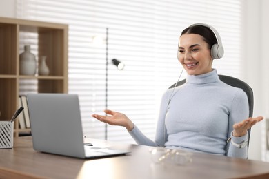 Young woman in headphones using video chat during webinar at table in office