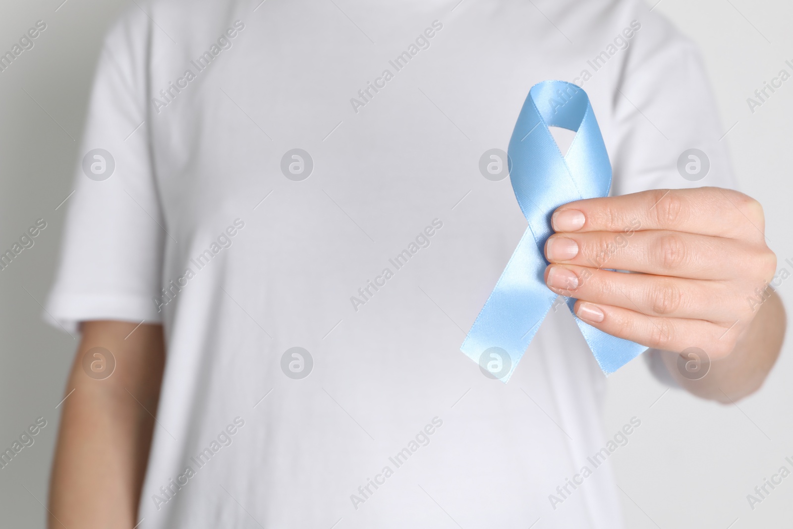 Photo of International Psoriasis Day. Woman with light blue ribbon as symbol of support on white background, closeup