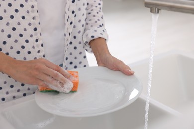 Photo of Woman washing plate above sink in modern kitchen, closeup