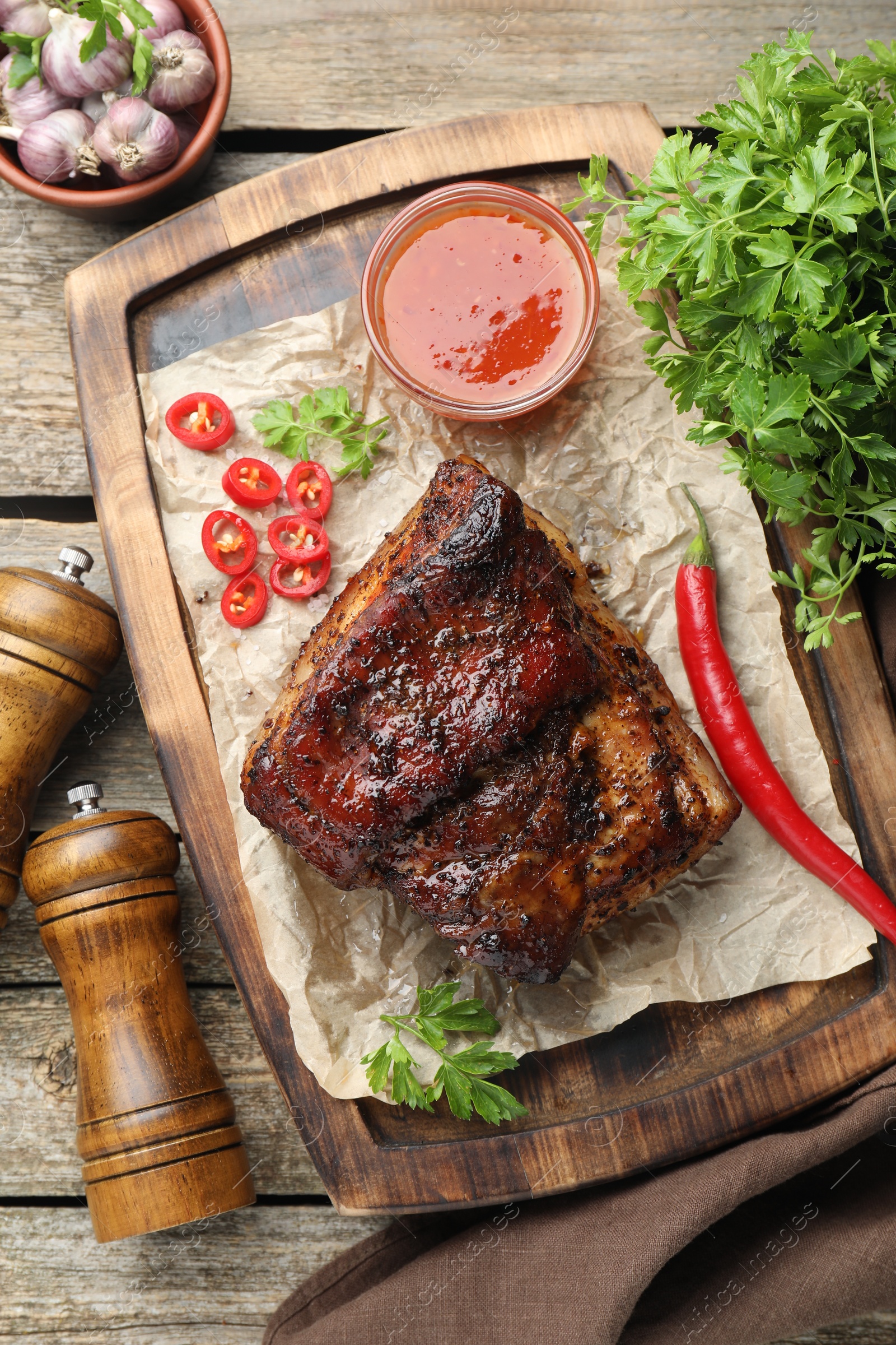 Photo of Piece of baked pork belly served with sauce and chili pepper on wooden table, flat lay