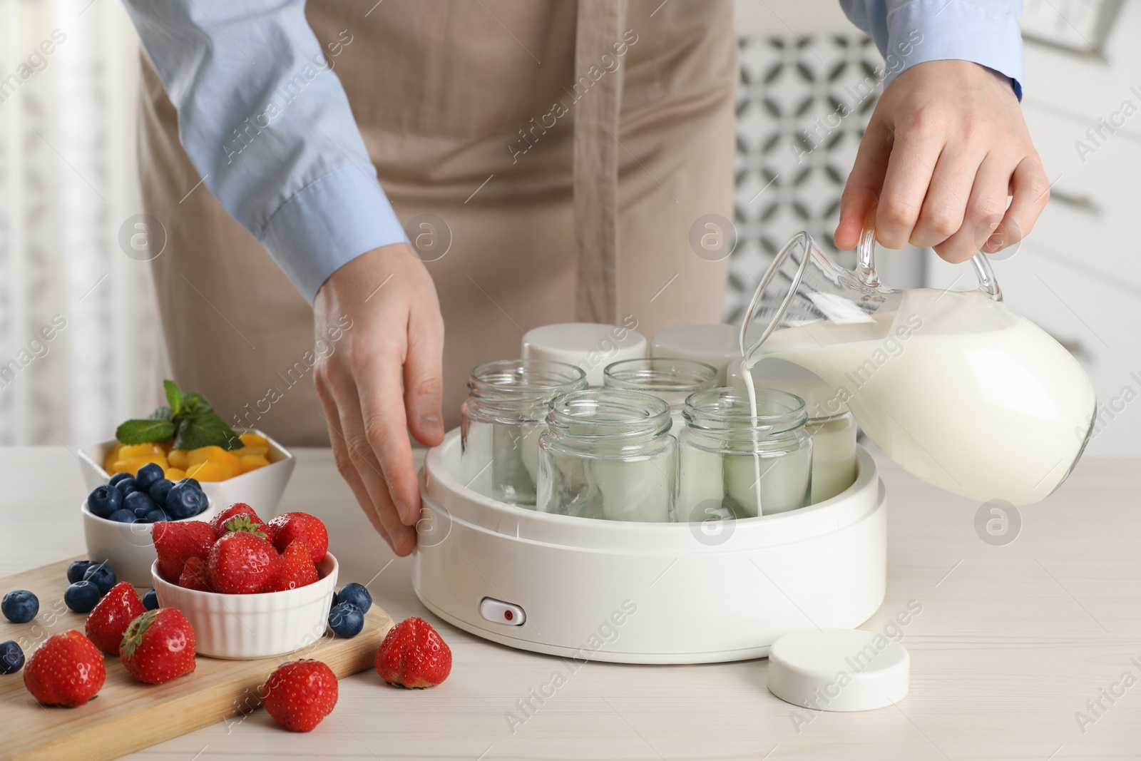 Photo of Woman making tasty yogurt at white wooden table in kitchen, closeup