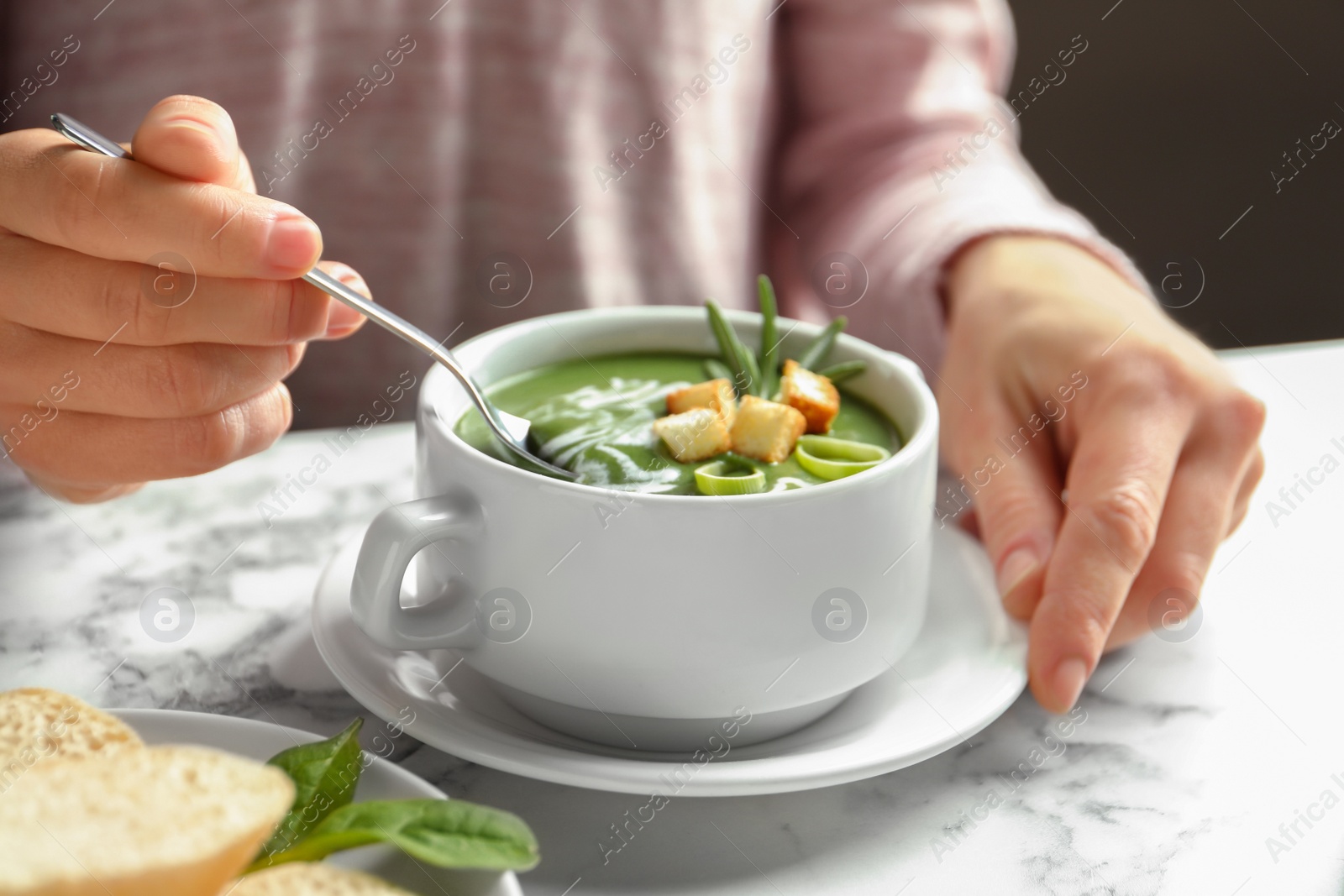 Photo of Woman eating fresh vegetable detox soup with croutons at table, closeup