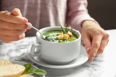 Photo of Woman eating fresh vegetable detox soup with croutons at table, closeup