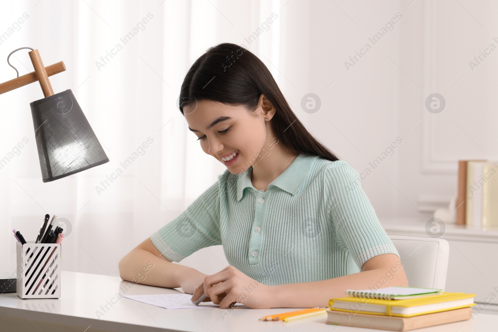 Photo of Teenage girl erasing mistake in her notebook at white desk indoors