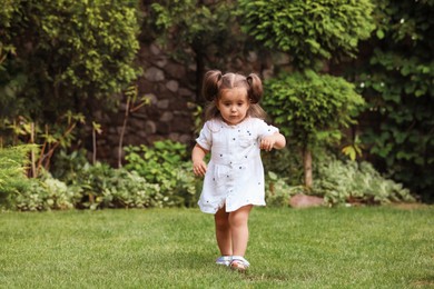 Cute little girl walking on green grass in park