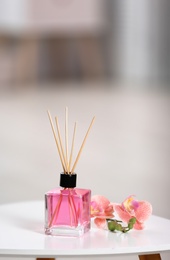 Photo of Aromatic reed air freshener and flowers on table against blurred background