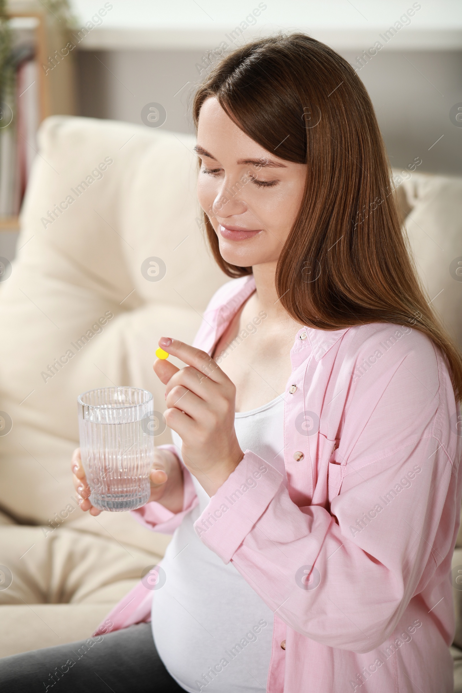 Photo of Beautiful pregnant woman holding pill and glass of water at home