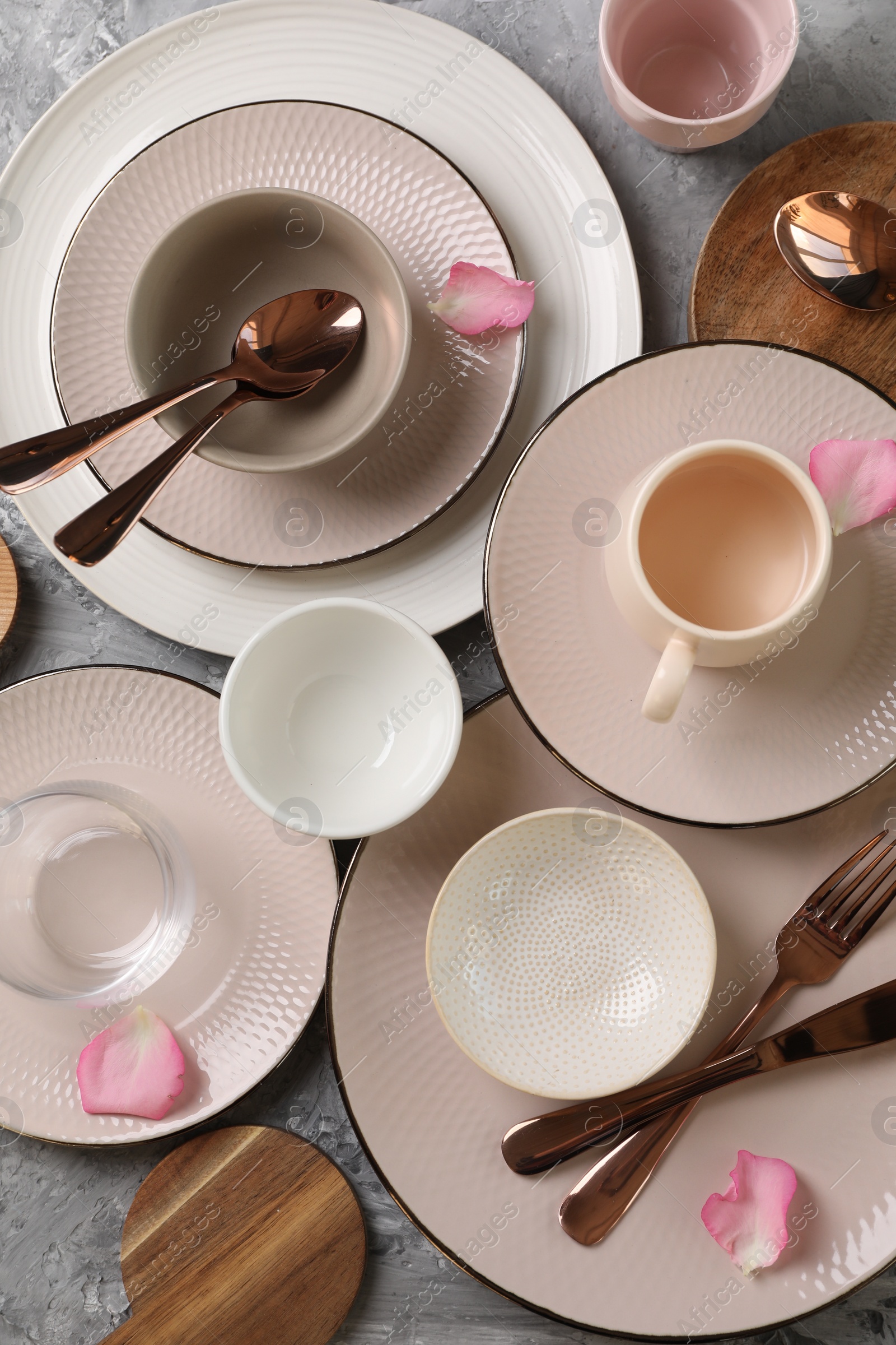 Photo of Stylish table setting. Dishes, cutlery, cup and petals on grey surface, flat lay