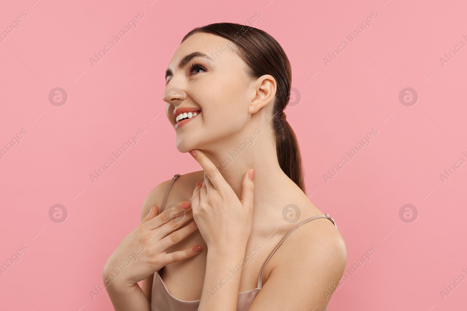 Photo of Smiling woman touching her neck on pink background