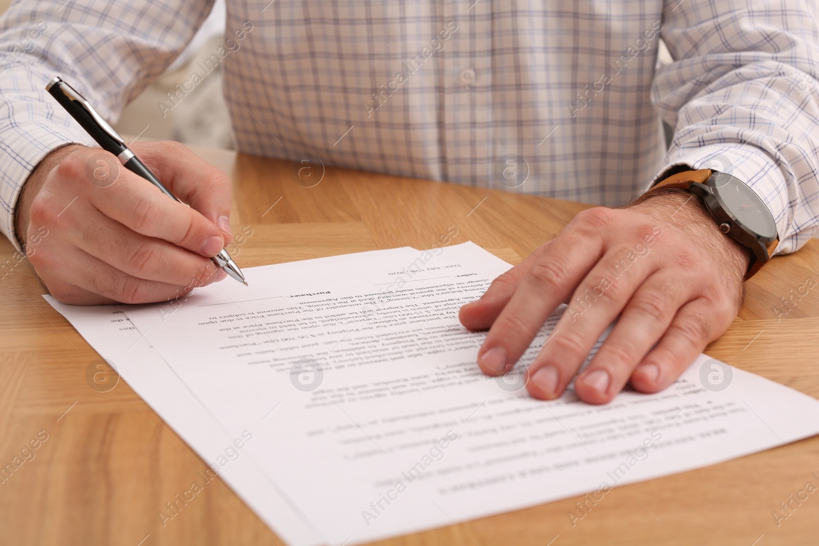 Photo of Businessman signing contract at wooden table, closeup of hands