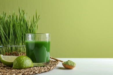 Photo of Composition with glass of wheat grass juice and lime on table against green background. Space for text