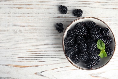 Photo of Bowl of ripe blackberries with mint on white wooden table, flat lay