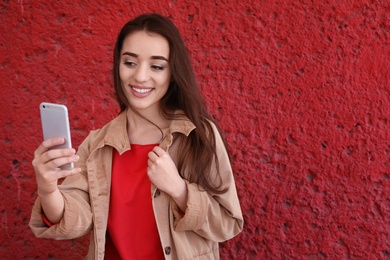 Photo of Attractive young woman taking selfie with phone on color background