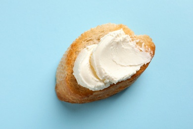 Photo of Piece of baguette with tasty cream cheese on color background, top view