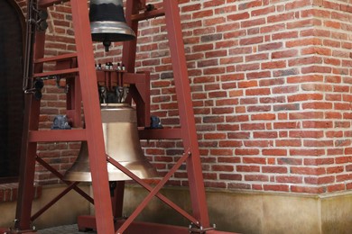 Photo of Wooden construction with two old bells near brick wall outdoors