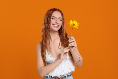 Photo of Beautiful young hippie woman with sunflower on orange background