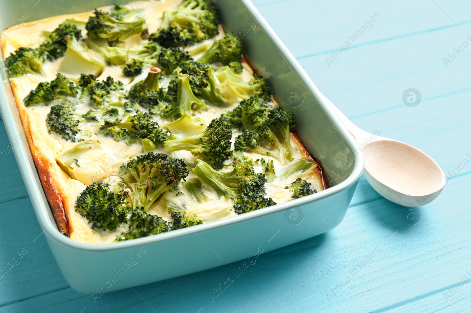 Photo of Tasty broccoli casserole in baking dish on blue wooden table