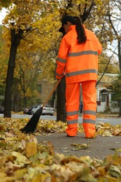 Photo of Street cleaner sweeping fallen leaves outdoors on autumn day, back view